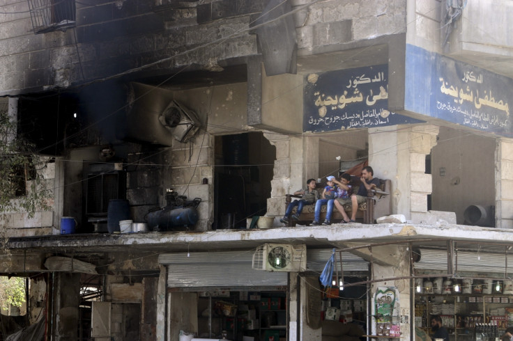 Aleppo resident sit outside damaged building