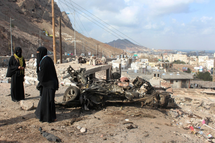 Yemeni women stand next to the remains of a vehicle