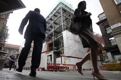 Pedestians walk past a building under construction in central London