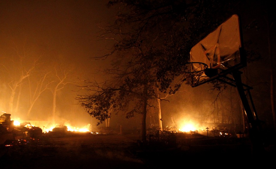 A basketball net can be seen in the foreground as a home burns near Bastrop