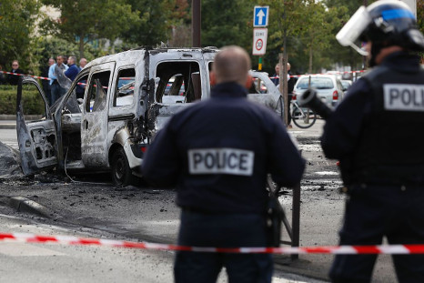 Police stand guard near a burned police vehicle (back) and a van in Viry-Chatillon