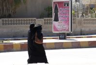Veiled women walk past a billboard that carries a verse from Koran urging women to wear a hijab in the northern province of Raqqa 