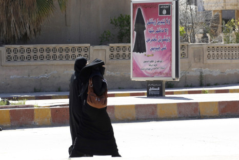 Veiled women walk past a billboard that carries a verse from Koran urging women to wear a hijab in the northern province of Raqqa 