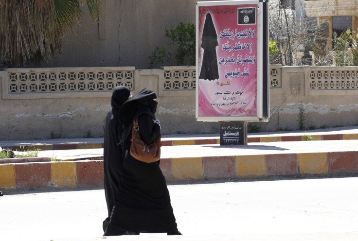 Veiled women walk past a billboard that carries a verse from Koran urging women to wear a hijab in the northern province of Raqqa 