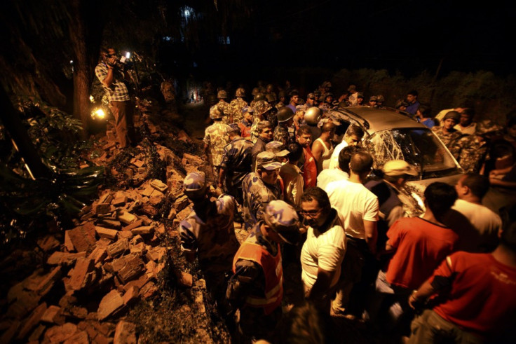 Members of the Nepalese army gather around a damaged car after the wall surrounding the British Embassy collapsed on top of the car that was passing by in Kathmandu