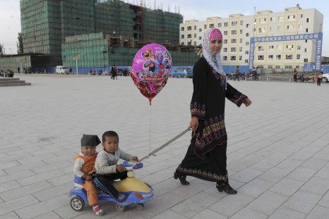 A Uighur woman pulls a buggy carrying her sons as she walks past residential buildings under construction in Uqturpan county, Xinjiang 