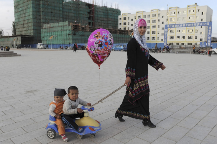 A Uighur woman pulls a buggy carrying her sons as she walks past residential buildings under construction in Uqturpan county, Xinjiang 
