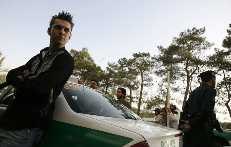 A youth leans against a police car after being detained for a Western-style haircut in Tehran