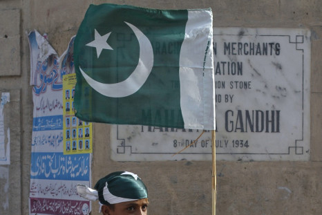 A boy ties up a Pakistan national flag to a bamboo stick as some of nearly a dozen traders near by taking part in an anti-American demonstration in Karachi