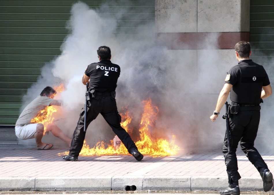 A policeman tries to extinguish a fire on a man after he set himself ablaze outside a bank branch in Thessaloniki in northern Greece