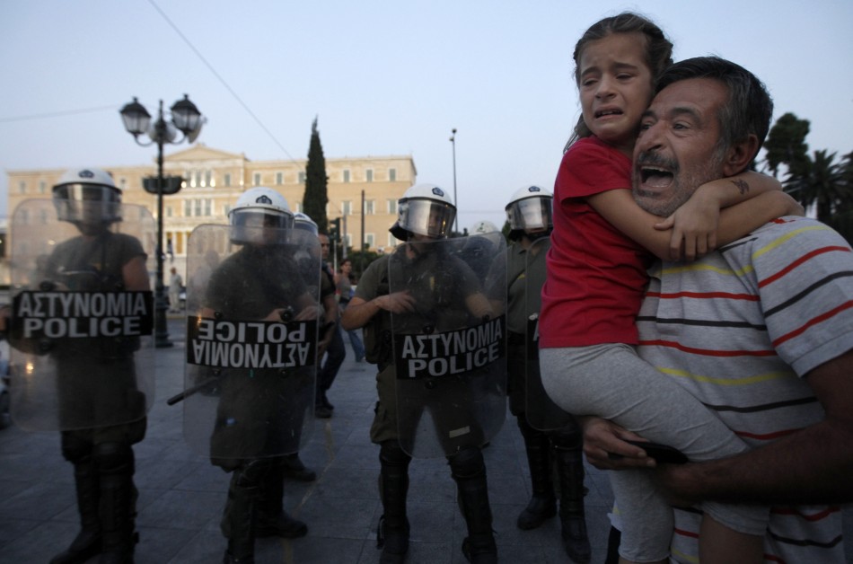 A protester, with a crying girl in his arms, shouts at riot police during a rally in Athens