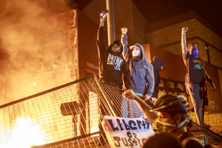 Protesters hold up their fists as flames rise behind them