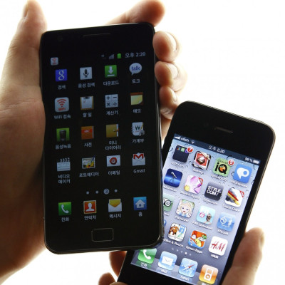 An South Korean mobile carrier employee holds an iPhone 4 and a Galaxy S II next to each other. Both phones feature better graphics, faster processors, voice assistants, and incredible cameras.
