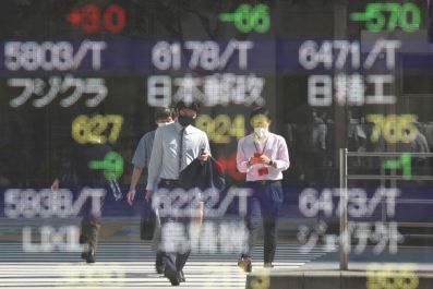 People wearing protective masks are reflected on an electronic board displaying Japan's stock prices outside a brokerage in Tokyo