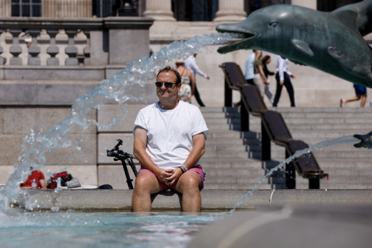 A man cools off in a fountain during the hot weather in London, Britain