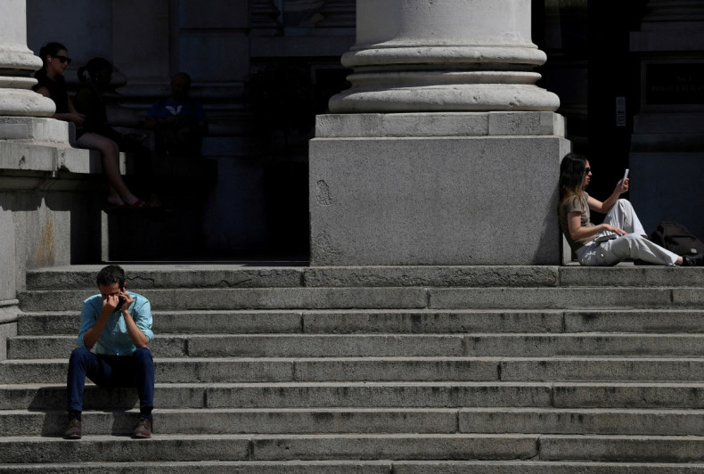 People sit outside near the Bank of England during the hot weather in the City of London financial district, London