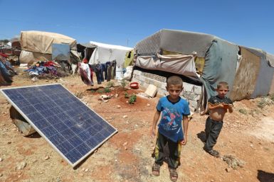 Children stand near a solar panel at a camp for Syrians displaced by conflict, near the Syrian border with Turkey in the rebel-held northern part of Idlib province