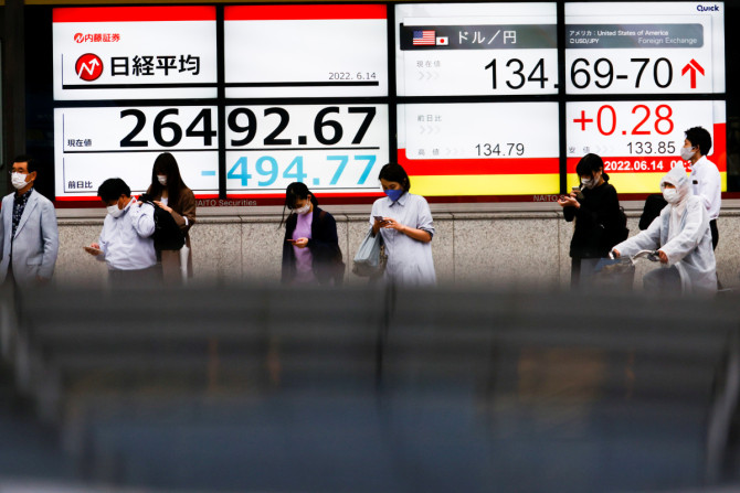 Passersby are seen in front of a screen displaying the Japanese yen exchange rate against the U.S. dollar and Nikkei share average in Tokyo