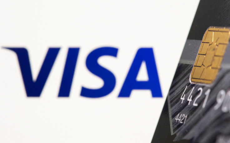 Credit card is seen in front of displayed Visa logo in this illustration