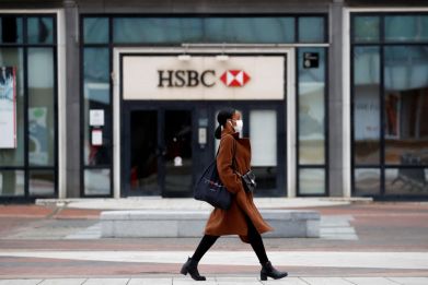 A woman wearing a protective face mask walks past a logo of HSBC bank at the financial and business district of La Defense near Paris