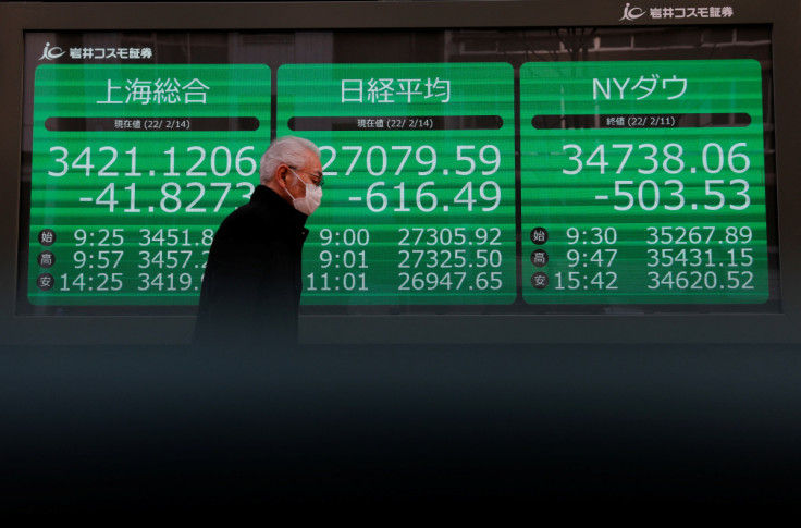 A man wearing a protective face mask walks past a screen outside a brokerage in Tokyo