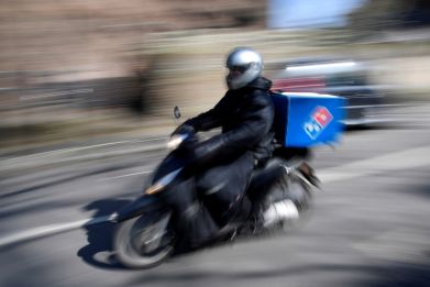 A Domino's pizza delivery driver rides a motorbike in a residential street in West London