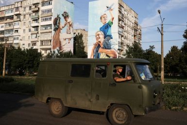 Ukraine servicemen drive past a graffiti of a family painted on damaged buildings in Bakhmut