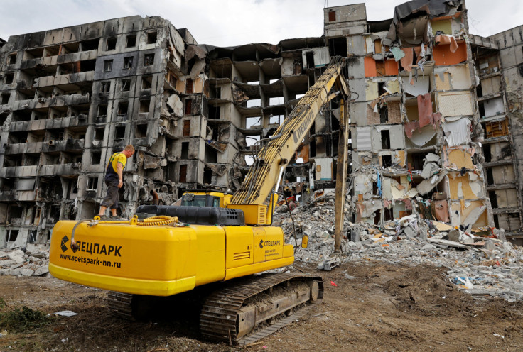 A worker stands on an excavator in front of a destroyed apartment building in Mariupol