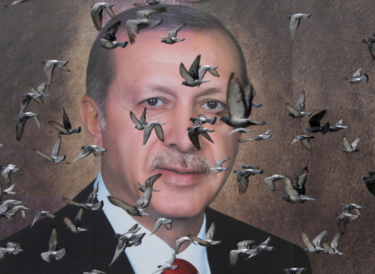 Pigeons fly in front of a large poster of Turkish President Tayyip Erdogan in Bursa