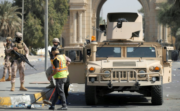 Municipality workers clean up as soldiers guard the entrance to the Green Zone