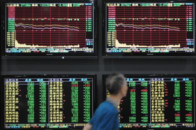 Man walks past screens showing stock information at a brokerage house in Jiujiang