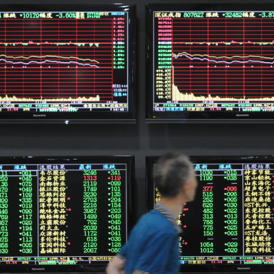 Man walks past screens showing stock information at a brokerage house in Jiujiang