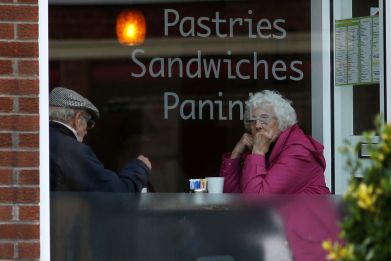 An elderly couple sit inside a coffee shop