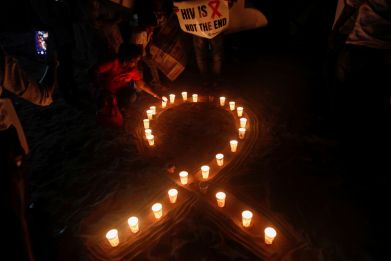 A woman arranges candles in the formation of a ribbon, the symbol for the solidarity of people living with AIDS on World AIDS Day on a beach in Mumbai