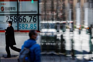 Passersby wearing protective face masks walk past a stock quotation board, in Tokyo