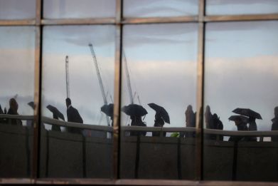 Commuters, reflected in windows of an office, walk across London Bridge toward the financial district, in London