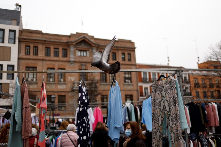 A pigeon flies past shoppers at a street market in Madrid