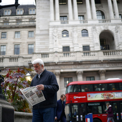 A person reads a newspaper outside the Bank of England in the City of London financial district in London