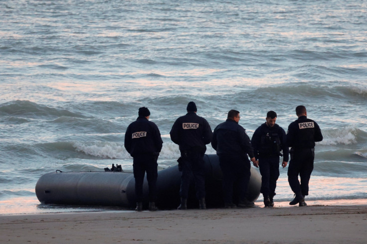 French policemen stand beside a dinghy lying on the beach after migrants tried to reach Britain