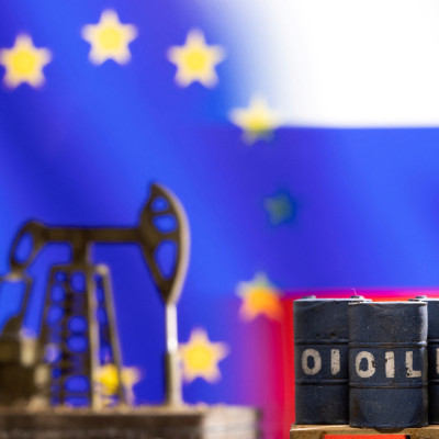 Illustration shows models of oil barrels and a pump jack in front of U.S. and Russia flag colors