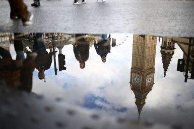 The Elizabeth Tower, more commonly known as Big Ben, is seen reflected in a puddle as people walk outside the Houses of Parliament in London