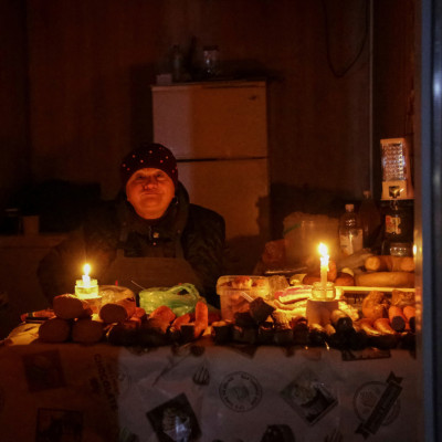 A vendor waits for customers in a small store, lit with candles during a power outage, after critical civil infrastructure was hit by Russian missile attacks in Odesa