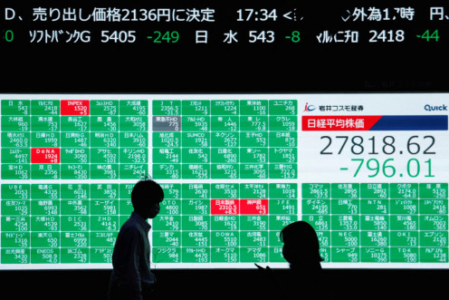 People walk past an electric board showing Japan's Nikkei share average in Tokyo