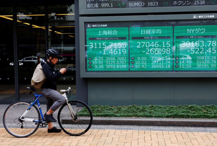 A man on a bicycle stands in front of an electronic board showing Shanghai stock index, Nikkei share price index and  Dow Jones Industrial Average outside a brokerage in Tokyo