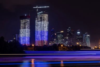 A high-rise apartment block under construction illuminated in colours of Russian flag is seen next to skyscrapers of Moscow International Business Centre in Moscow