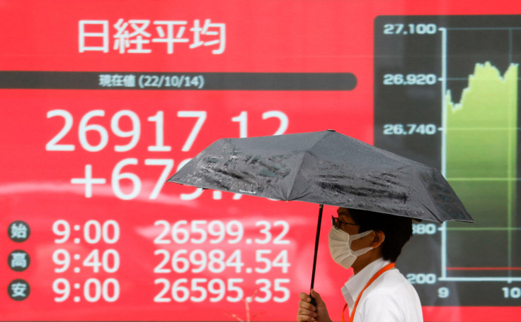 A man walks past in front of an electric monitor displaying the Japanese Nikkei share average in Tokyo