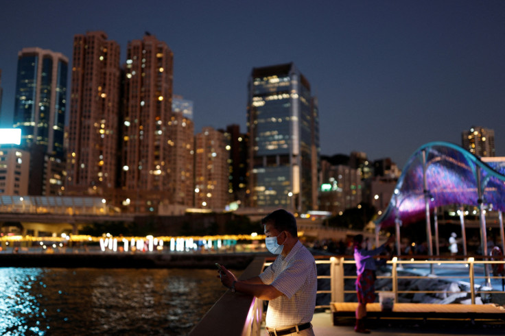 A man checks his phone at a promenade during sunset in Hong Kong