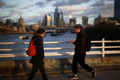 People walk across Waterloo Bridge with the City of London financial district in the background, in London