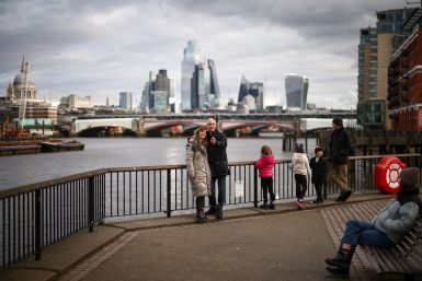 People take a selfie next to the bank of the River Thames, with the City of London financial district in the background, in London