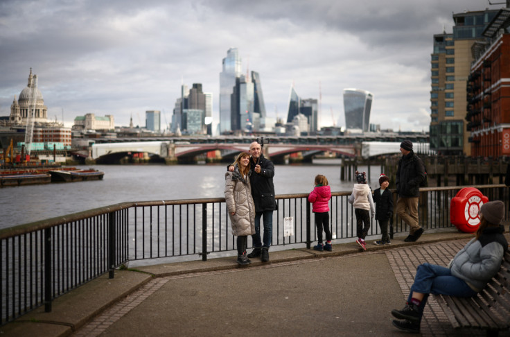People take a selfie next to the bank of the River Thames, with the City of London financial district in the background, in London